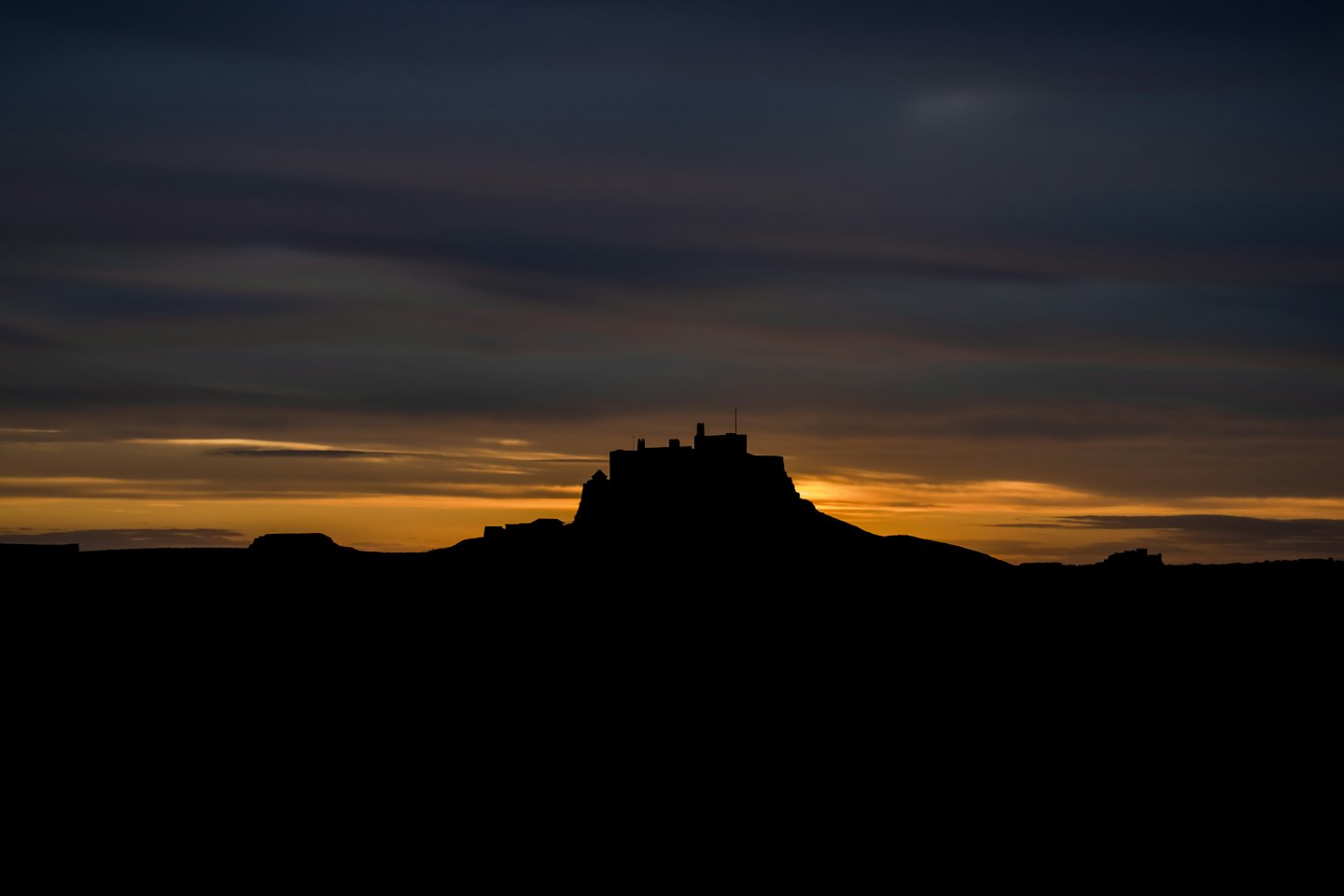 Silhouette einer historischen Burg auf einem grasbewachsenen Hügel.